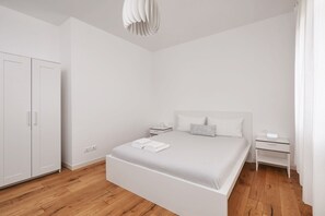 A minimalist bedroom with a large bed, white wardrobe, bedside tables, and a modern light fixture. - A cozy and private apartment situated in the heart of Venice Mestre. (Venezia)