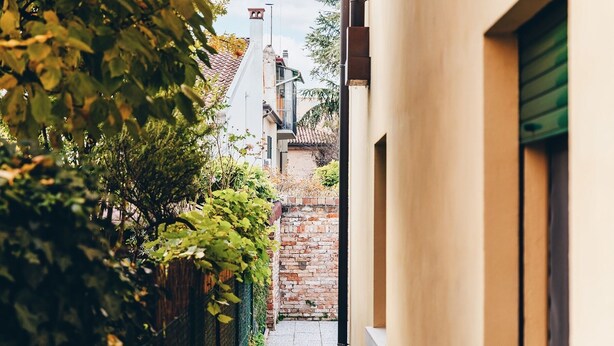 A narrow alleyway with a brick wall and a building with a green shutter on the right.