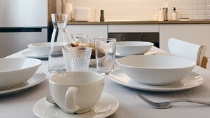 A modern kitchen with white appliances, a white brick backsplash, and a dining table set with white bowls, cups, and a glass pitcher.