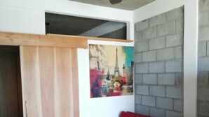 Een kamer met een rode bank, een plafondventilator, een schilderij van de Eiffeltoren en een grijze bakstenen muur.