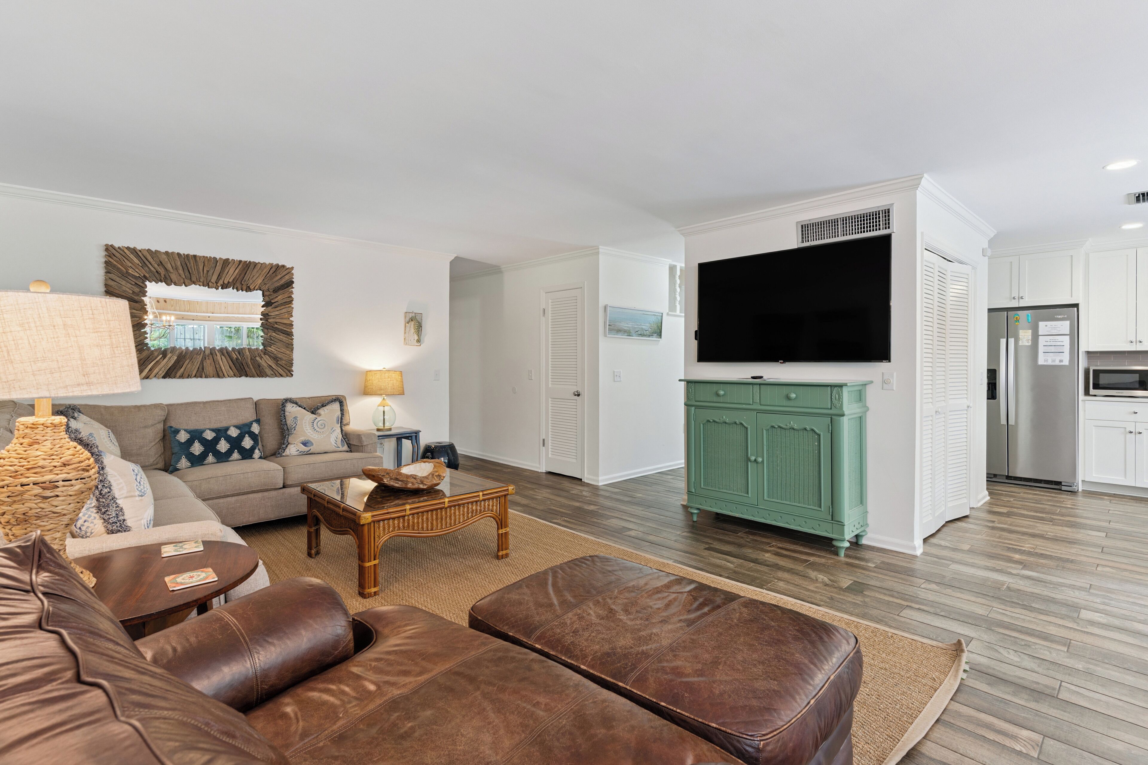 A living room with a sofa, coffee table, and ottoman, a kitchen with a TV, and a dining area with a table and chairs.