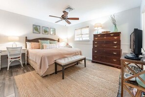Um quarto com cama, cômoda, cadeira, televisão e ventilador de teto.