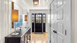A hallway with a wooden herringbone floor, a black door with glass panels, and a wall-mounted lamp with a ship painting. - Historic home in seaside village of Swansboro w/ private beach parking  (Swansboro)