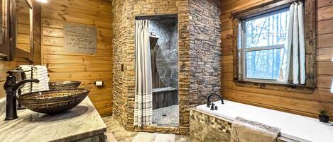 Un baño rústico con ducha de piedra, un lavabo grande tipo cuenco y una ventana con cortinas.