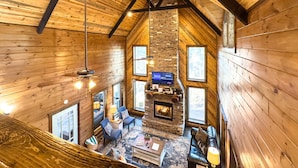 A cozy cabin interior with a stone fireplace, wooden walls, and a television. - The Good Stuff - Zipline, Gameroom, Hot Tub, & Firepit. 8 Beds / Sleeps 12 (Broken Bow)