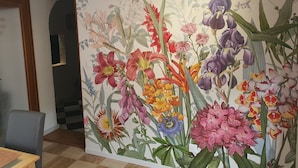 Une pièce avec un grand décor mural représentant des motifs floraux, une porte en bois et un sol à carreaux.