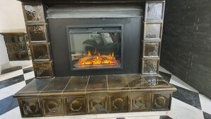 Une cheminée avec une façade en verre, entourée de carreaux décoratifs et surmontée d’un sol à carreaux noirs et blancs.
