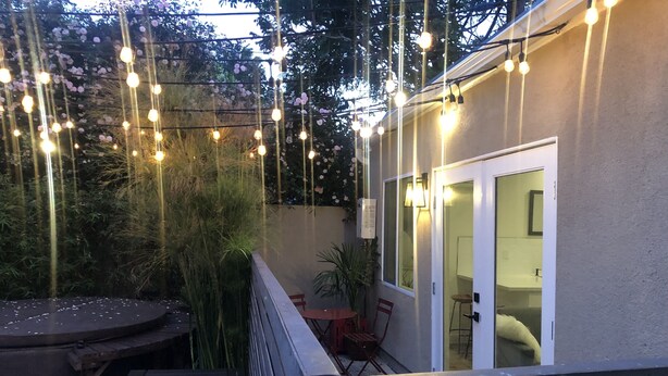 Een terras buiten met een ronde tafel en stoelen, lichtjes en een houten terras.