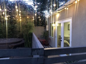 Un espace extérieur aménagé en terrasse, avec une table ronde et des chaises, des guirlandes lumineuses et une plateforme en bois.