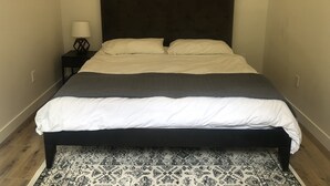 Een bed met een donker hoofdbord, wit-grijs beddengoed en een kamerkleed met een patroon.