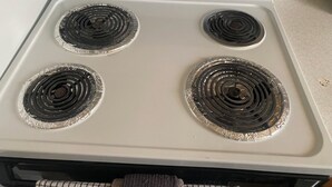 Una estufa blanca con cuatro quemadores, cada uno cubierto con papel de aluminio.