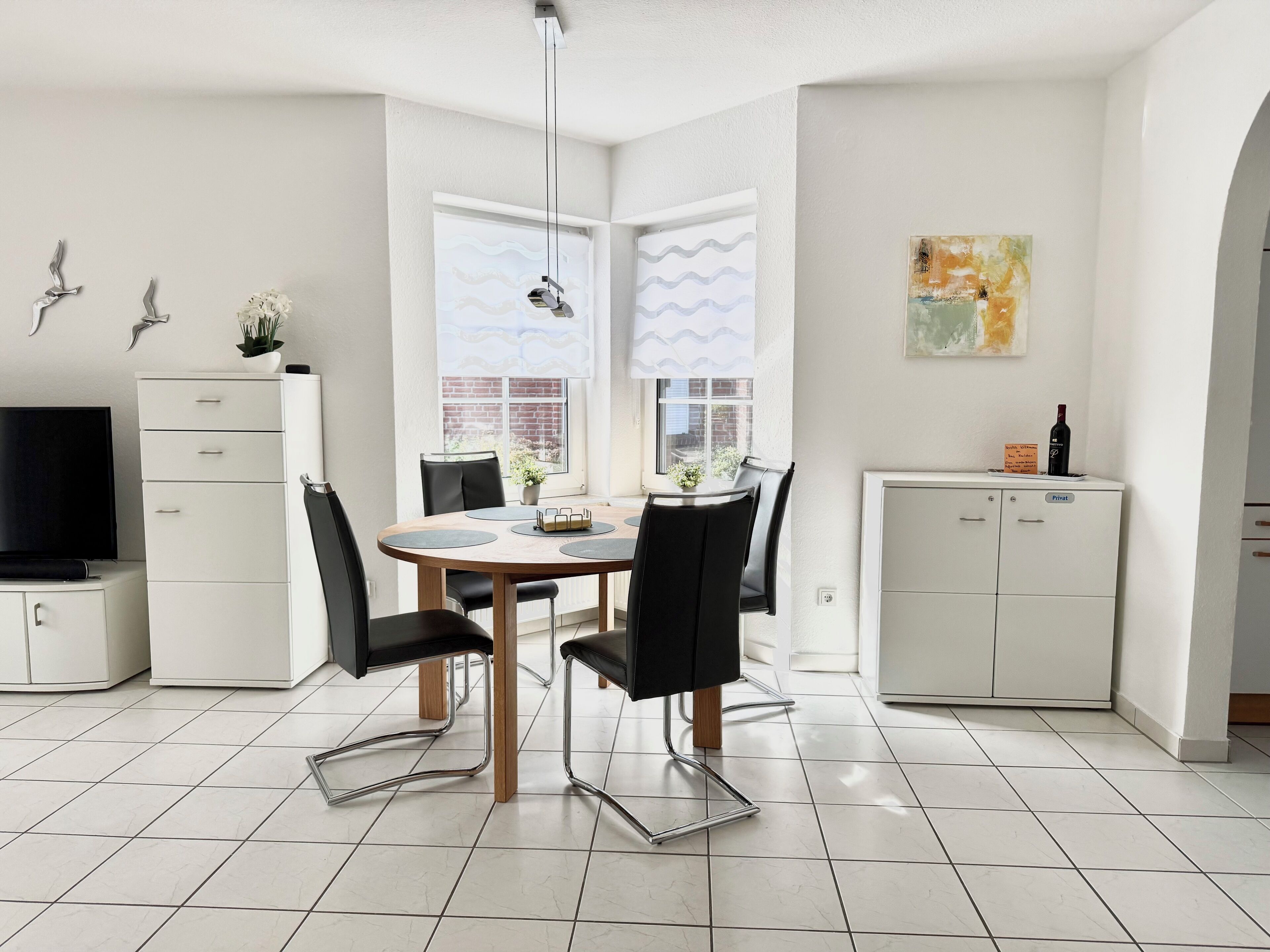 A modern kitchen with white cabinets, a dining table with chairs, and a TV on the left.