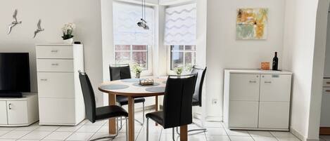 A modern kitchen with white cabinets, a dining table with chairs, and a TV on the left.