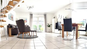A spacious living area with a modern chair, a dining table, and a staircase.
