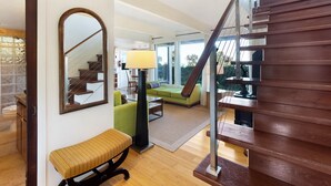 A spacious living area with a staircase, a green sofa, a bench, and a large mirror. - Rustic yet modern Upcountry retreat with breathtaking views! (Makawao)