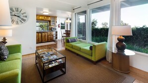 A spacious living room with a green sofa, a coffee table, and a large wall clock. - Rustic yet modern Upcountry retreat with breathtaking views! (Makawao)