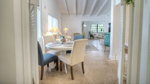 Un coin repas avec une table ronde, des chaises et un ventilateur de plafond. Il y a des fenêtres avec des stores et une vue sur l’extérieur.