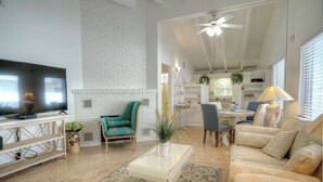 Un salon moderne doté d’un téléviseur à écran plat, d’un mur d’accent en briques blanches, d’un ventilateur de plafond et d’un coin repas avec une table et des chaises.