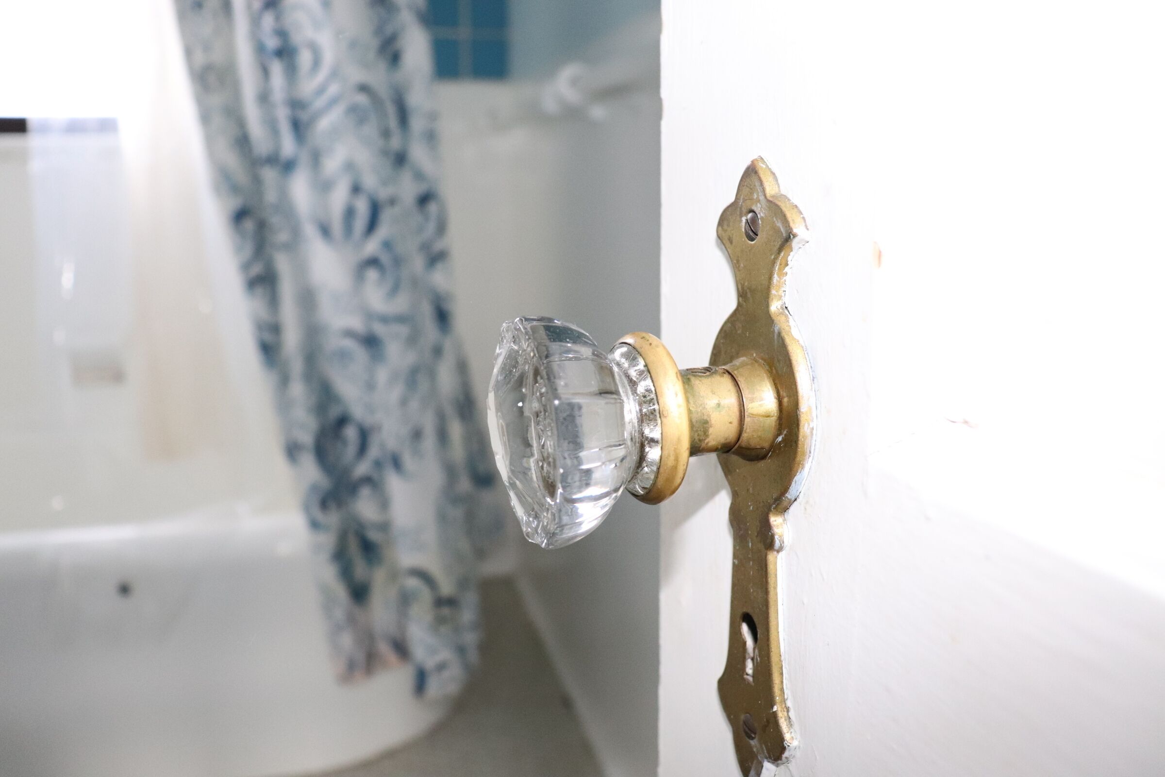 A bathroom with a white bathtub, a blue and white patterned shower curtain, and a brass faucet with a clear glass knob.