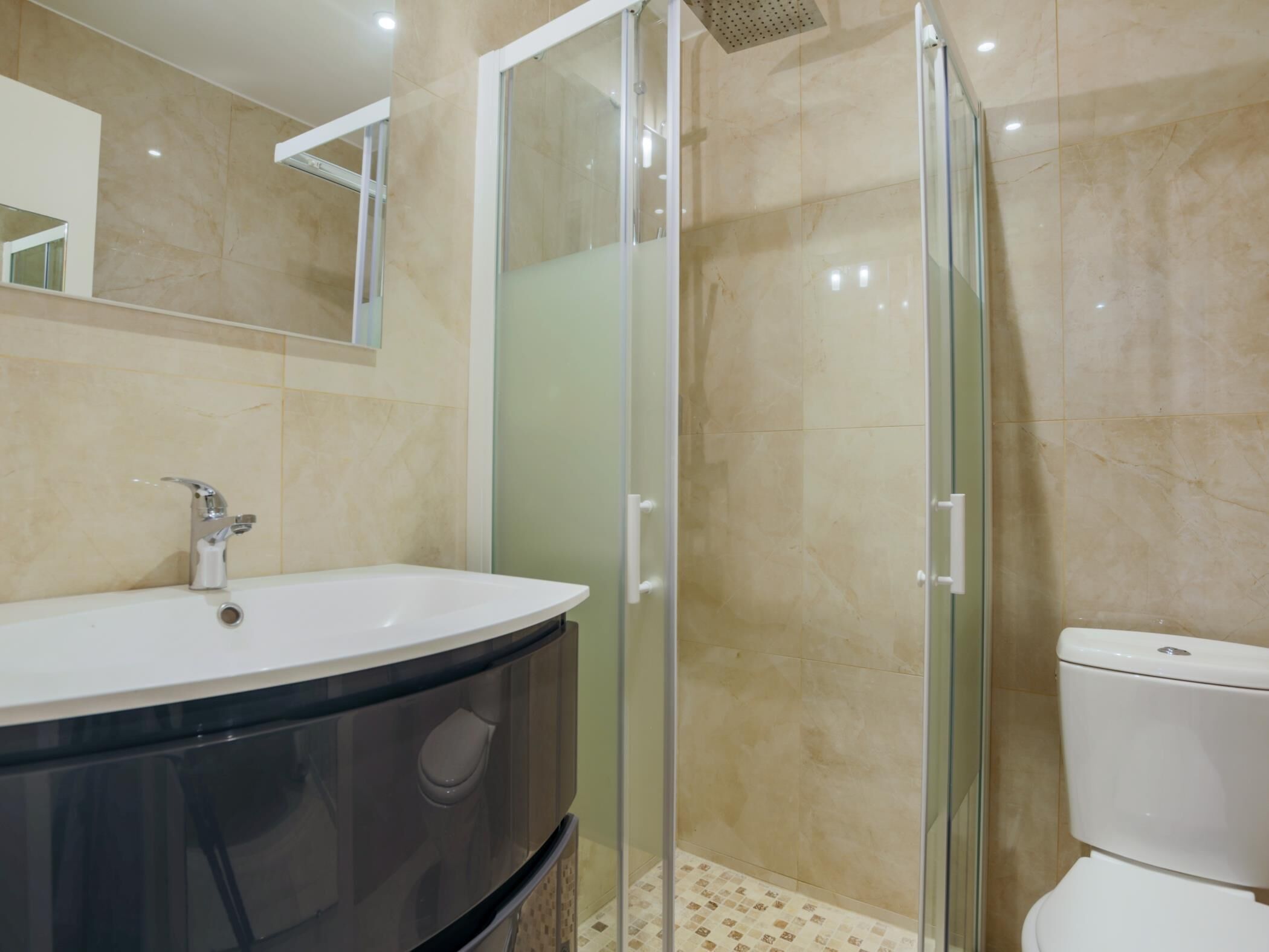 A modern bathroom with a glass shower enclosure, a white sink, and a toilet.