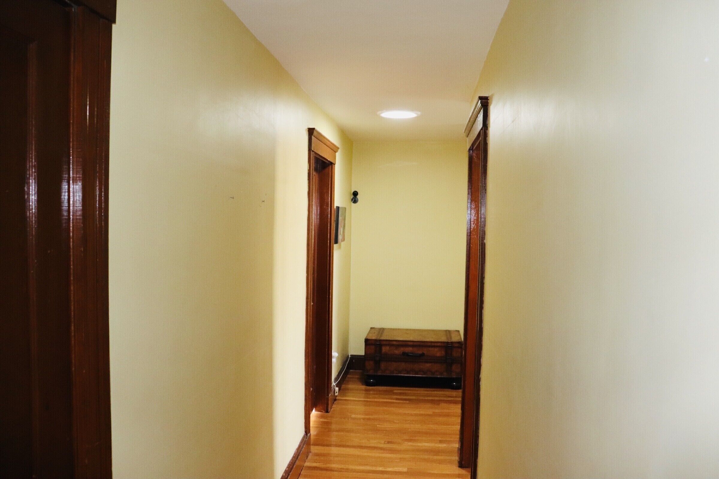 A narrow hallway with wooden flooring and yellow walls.