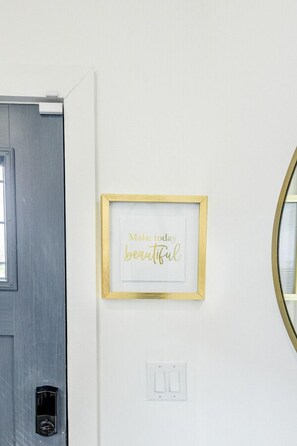 A door with a small window, a framed inspirational quote on the wall, and a light switch below it.
