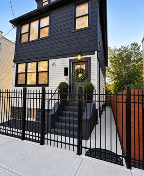 A two-story house with a black exterior, a front door with a wreath, and a black metal fence.