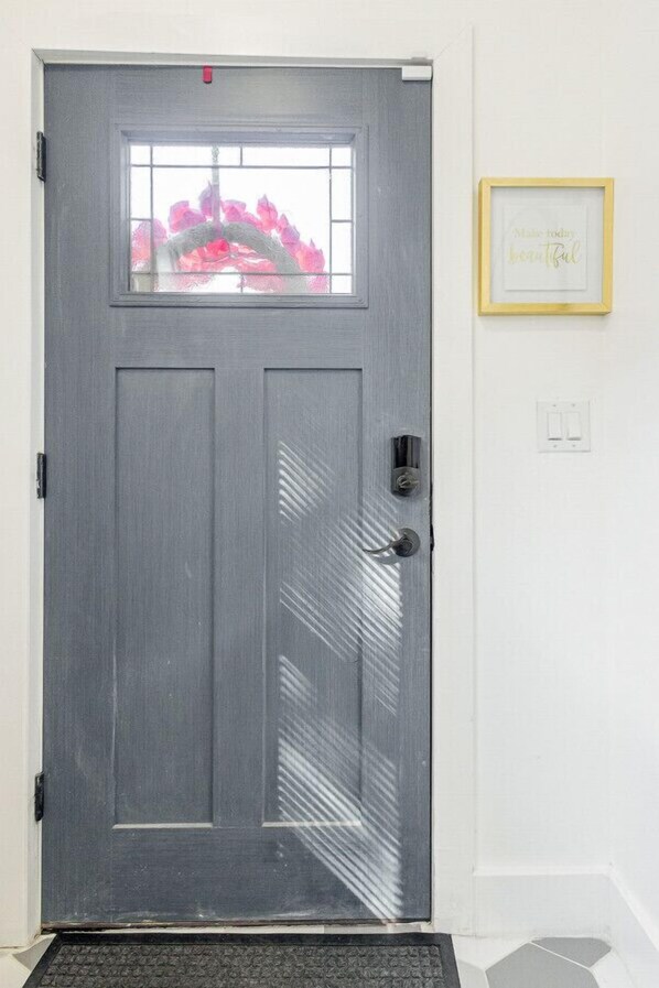 A gray door with a window, a doormat, and a framed inspirational quote on the wall.