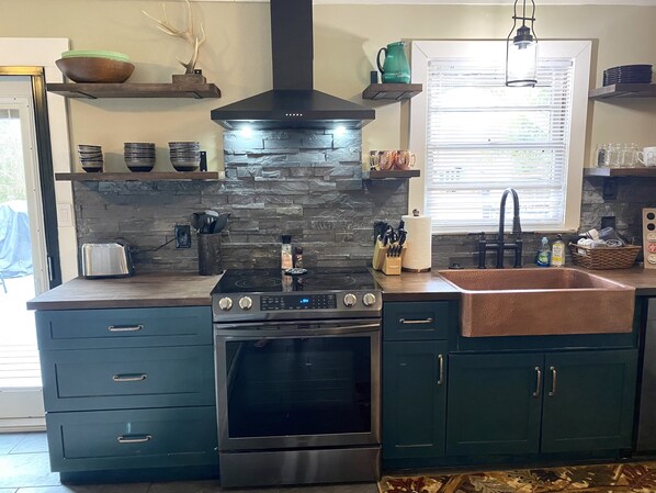 A kitchen with a stone backsplash, stainless steel appliances, and teal cabinetry.