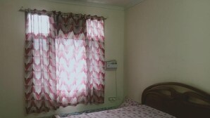 A bedroom with a bed, a window with patterned curtains, and a wall socket.