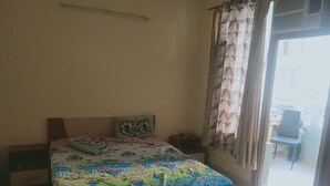 A bedroom with a bed, a nightstand, a window with curtains, and a view of the outside.