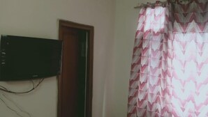 A room with a television mounted on the wall, a door, and patterned curtains.