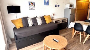 Un espacio habitable compacto con un sofá, una mesa redonda pequeña, un televisor y un microondas.