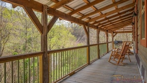 Une terrasse en bois surmontée d’un toit en métal, entourée d’arbres.
