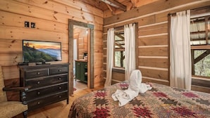Une chambre dans une cabane en bois, avec un lit, une commode et un téléviseur posé sur un meuble.