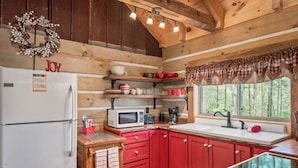 Une cuisine de style rustique équipée d’un réfrigérateur, d’un four à micro-ondes et de meubles de rangement rouges.