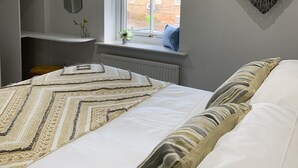 A bedroom with a bed, a window with curtains, a heart-shaped wall decoration, and a shelf with items.