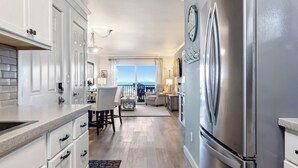 A modern kitchen with white cabinetry, a stainless steel refrigerator, and a wooden floor. - Upgraded for 2026 Huge Deck, Full-Size Pool, Beach Front, Linens Included (Carolina Beach)