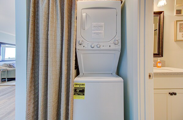 A front-loading washer and dryer in a room with a window, a mirror, and a countertop with a soap dispenser.