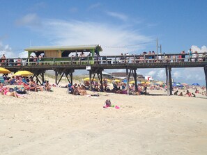 A beach with a wooden pier and beach umbrellas. - Upgraded for 2026 Huge Deck, Full-Size Pool, Beach Front, Linens Included (Carolina Beach)