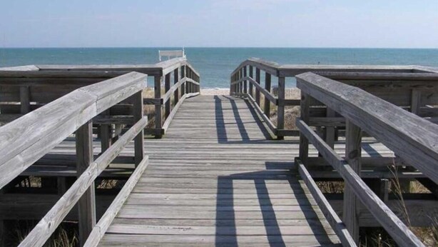 A wooden boardwalk leading to the beach with railings on both sides. - Upgraded for 2026 Huge Deck, Full-Size Pool, Beach Front, Linens Included (Carolina Beach)