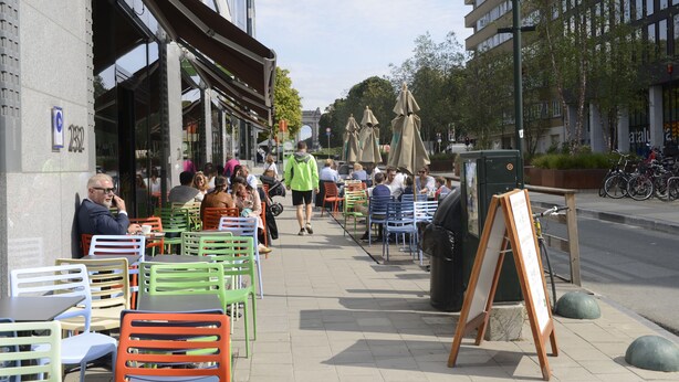 An outdoor café with tables and chairs, a signboard, and a bicycle parked nearby. - Fresh New EU COMMISSION area apartment  (Bruxelles)