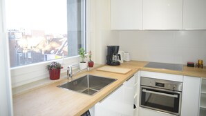 A modern kitchen with a large window, stainless steel sink, white cabinets, and a built-in oven. - Fresh New EU COMMISSION area apartment  (Bruxelles)