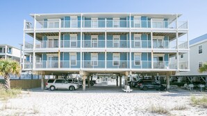Een meerlaags hotel aan het strand met balkons, een overdekte parkeerplaats en een zandstrand ervoor.