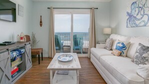 Een woonkamer met een witte bank, een salontafel, een televisie en een balkon met strandstoelen.