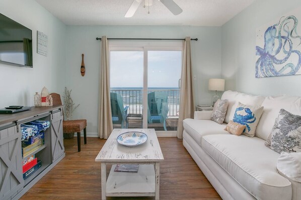 A living room with a white sofa, a coffee table, a TV, and a balcony with beach chairs. - Fall Sale! Aamazing View! 2BR/1B Gulf Front! (Gulf Shores)