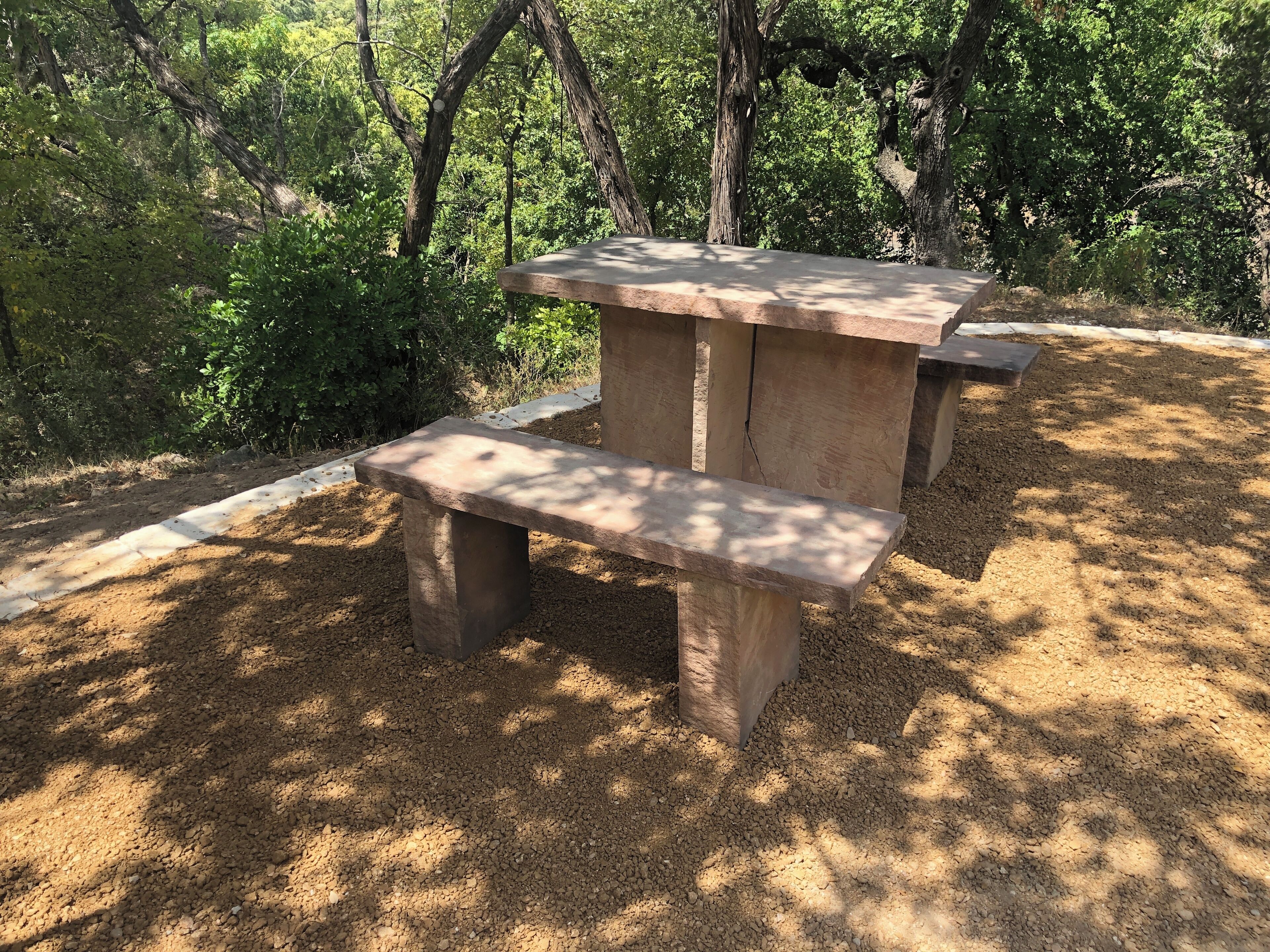 Una mesa de piedra con bancos en un área boscosa.