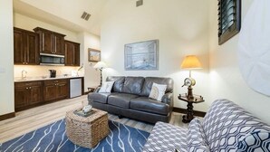 A compact living space with a kitchenette, a leather sofa, a patterned armchair, and a decorative lamp.