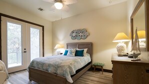 A bedroom with a bed, a nightstand, a lamp, a decorative wall piece, and a view through a door.
