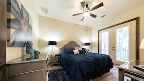 A bedroom with a large bed, two bedside lamps, a ceiling fan, and a view through a door.
